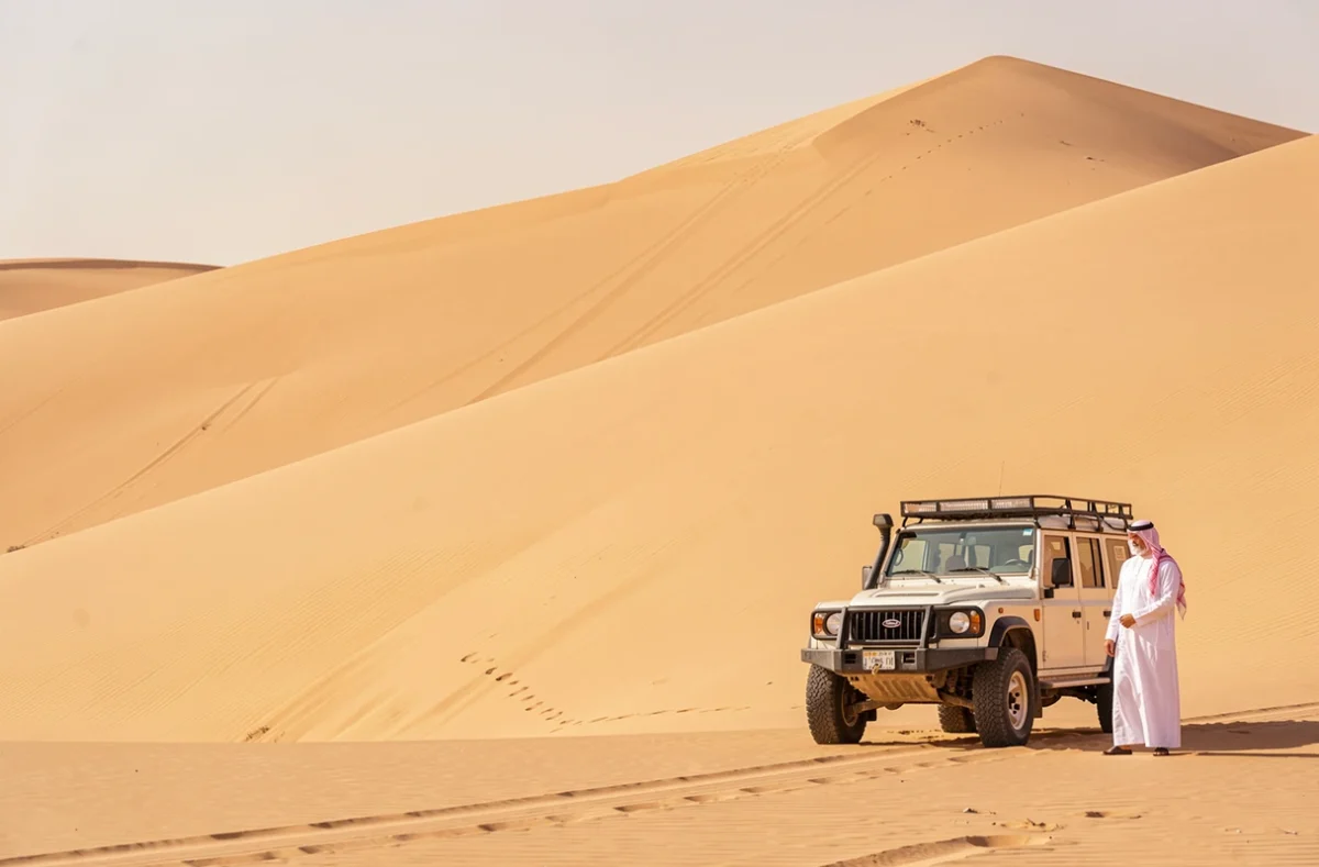 Homme en thobe blanc et ghutrah rouge face aux dunes immenses du Rub al Khali en Arabie saoudite