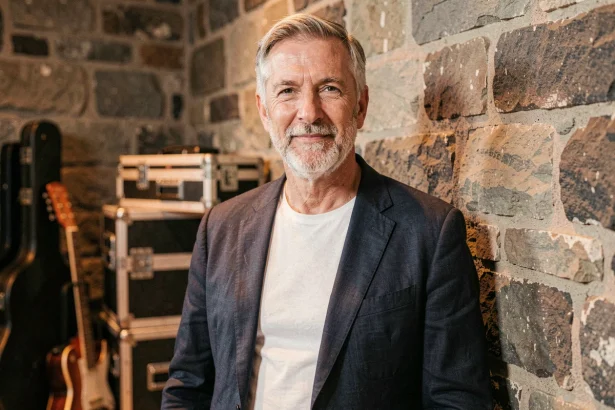 Portrait de Florent Pagny, chanteur français dans la soixantaine, cheveux grisonnants et barbe courte, veste en lin sombre, backstage d'une salle de concert