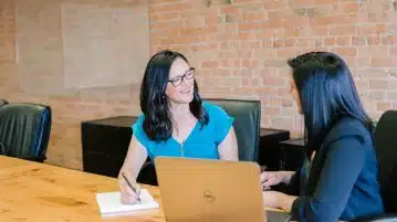 woman in teal t-shirt sitting beside woman in suit jacket